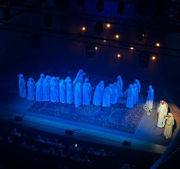 Group of people dressed in traditional attire on a stage under blue lighting.
