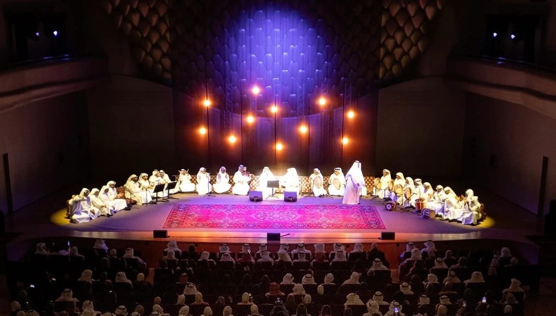 A group of performers dressed in white on a stage with an audience.