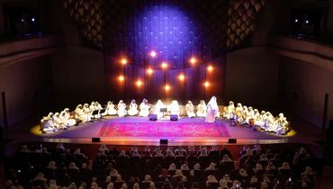 A group of performers dressed in white on a stage with an audience.