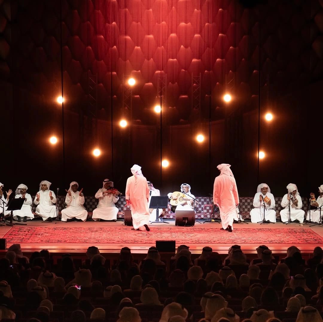 Traditional musical performance with musicians in white robes on stage.