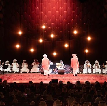 Traditional musical performance with musicians in white robes on stage.