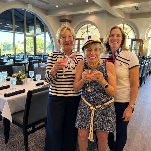 Three women posing with drinks at a nautical-themed event.