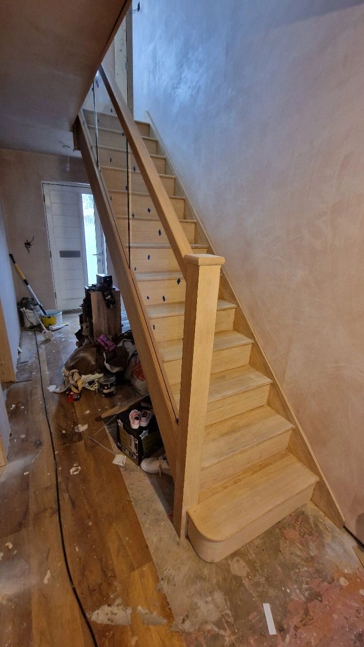 Newly installed wooden staircase with glass railing in a room under renovation.