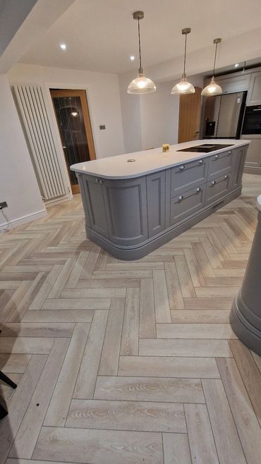 Modern kitchen with a gray island and wooden herringbone floor.