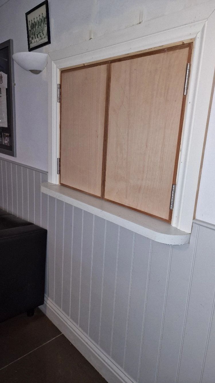 Wooden trapdoor on a white paneled wall with nearby furniture.