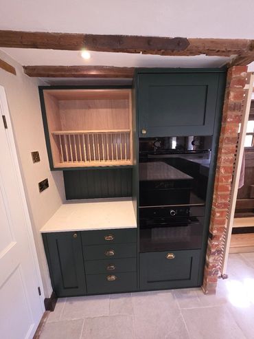 Dark green kitchen cabinets with built-in oven and wooden dish rack.
