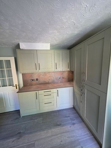 Modern kitchen cabinets with a textured wall and wooden floor.