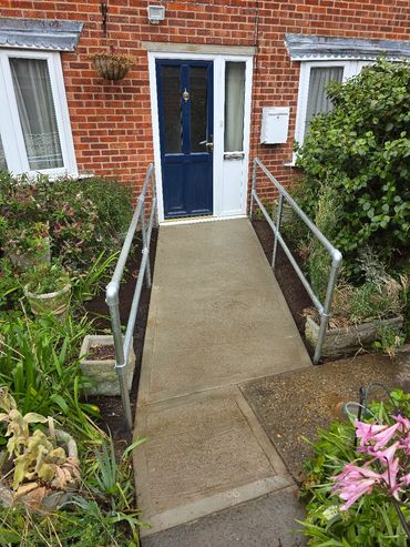 Concrete ramp with metal handrails leading to a blue door on a brick house.