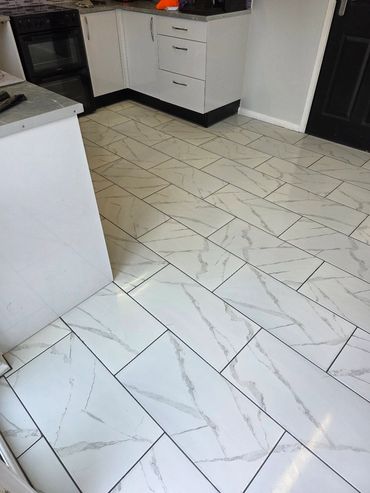 Kitchen floor with white marble-patterned tiles and white cabinets.