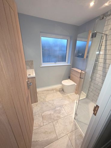 Modern bathroom with glass shower, tiled floor, and wood accents.