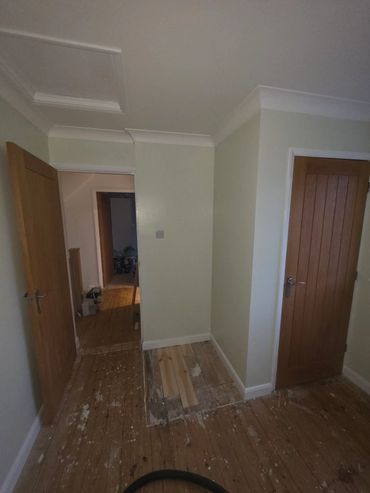A hallway with wooden doors and a worn wooden floor under renovation.