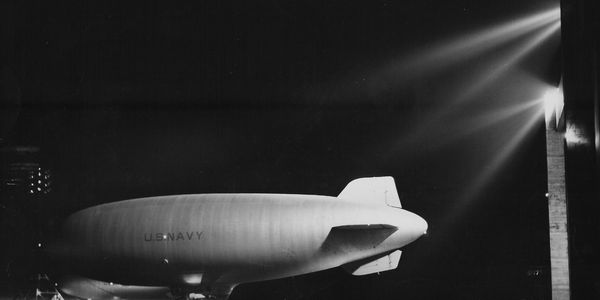 US Navy blimp at night under spotlight.
