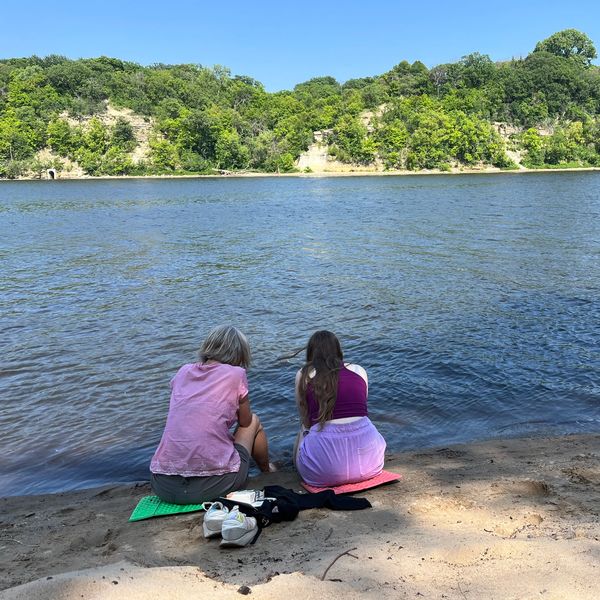Two people sitting by a riverbank on a sunny day.