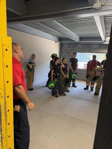 Group of firefighters in training holding helmets indoors.