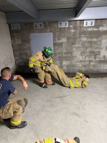 Firefighters training with a rescue drag technique in a concrete room.