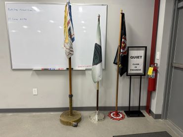 Three flags stand near a whiteboard and a quiet sign in a classroom.