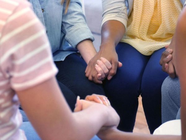 People holding hands in a supportive group setting.