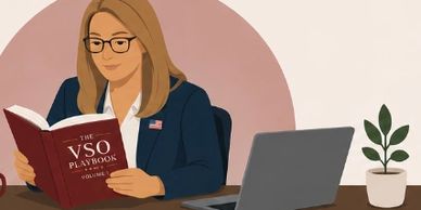 Woman reading a book titled 'The VSO Playbook' at a desk with a laptop.