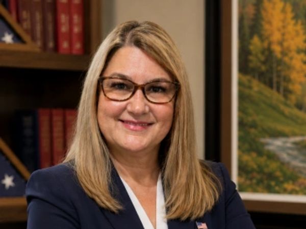 Professional woman in glasses and blazer smiling with arms crossed.
