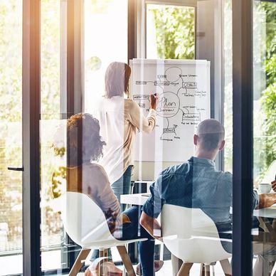 Personas en reunión de trabajo con planeación en pizarra.