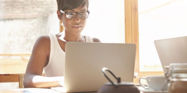 Woman working on laptop with glasses in a sunny room.
