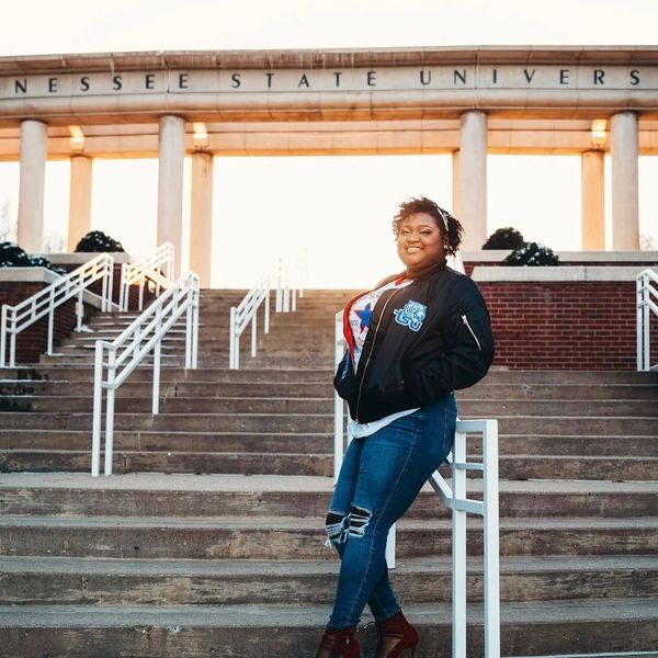 Young woman posing confidently on university steps at sunset.