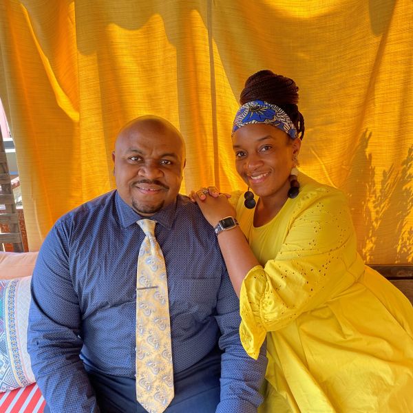 A smiling couple poses together with a bright yellow backdrop.