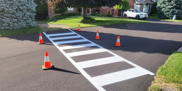 Freshly painted pedestrian crosswalk blocked by traffic cones on a residential street.