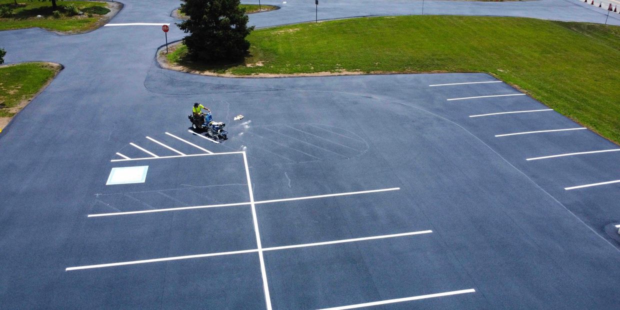 Worker painting fresh white lines in an empty parking lot.