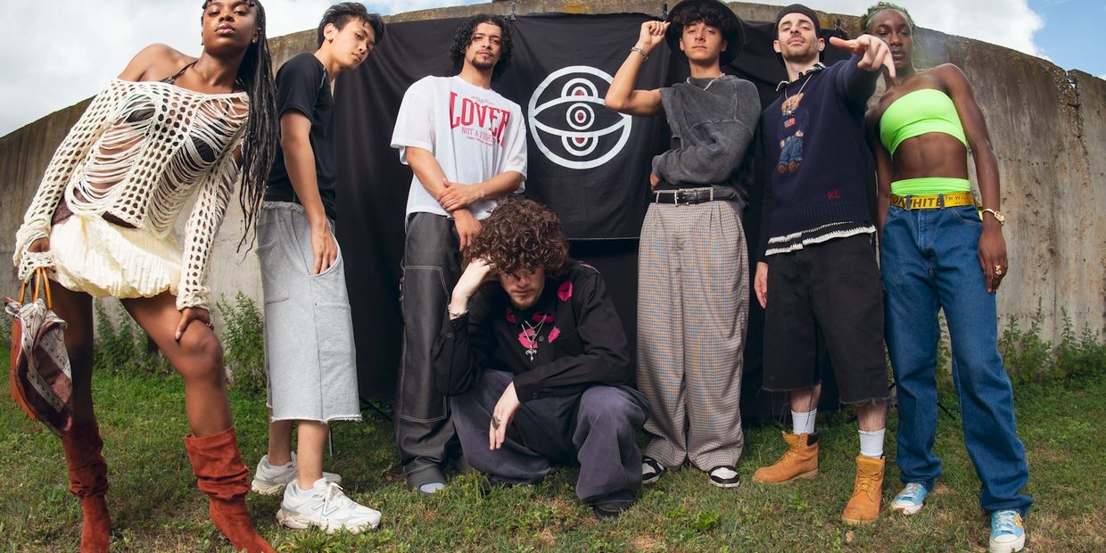 A diverse group of young adults posing outdoors in stylish, eclectic fashion against a black backdrop with a logo.