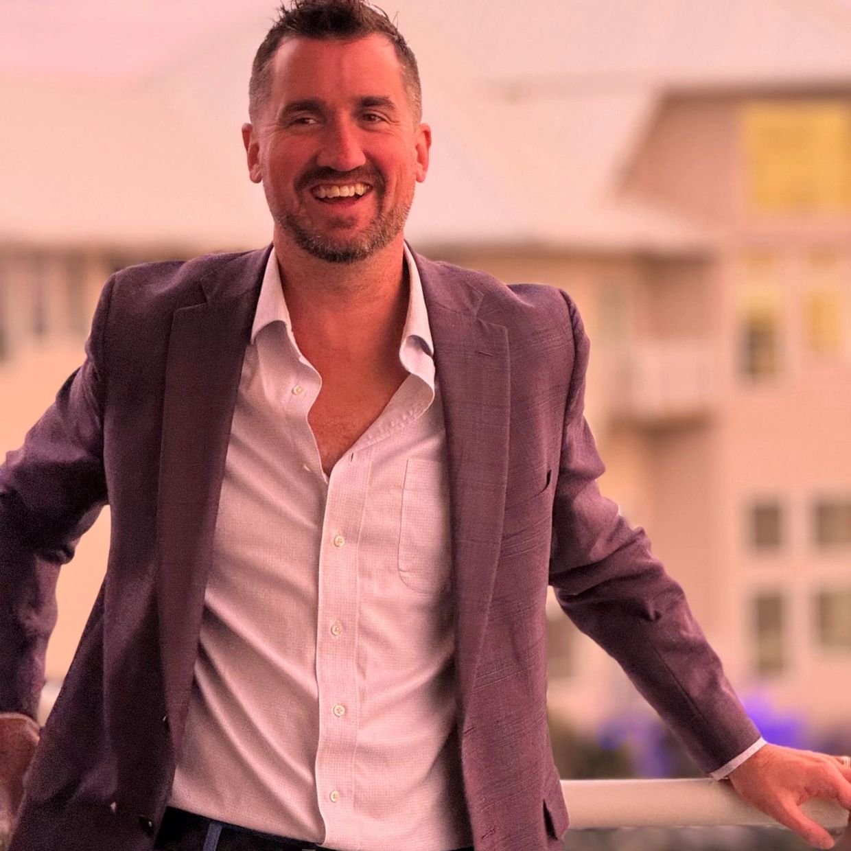 A man in a purple blazer and white shirt smiling outdoors.