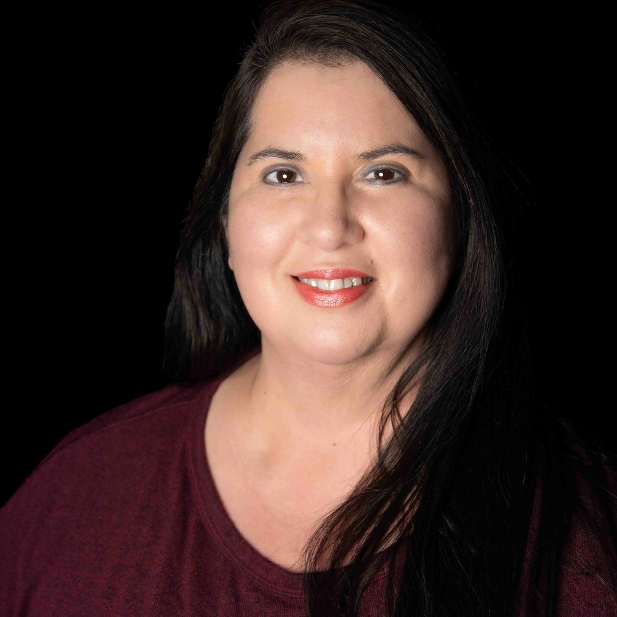 Smiling woman with long dark hair wearing a maroon top against a black background.