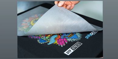 Person peeling off a transfer sheet from a colorful printed fabric.