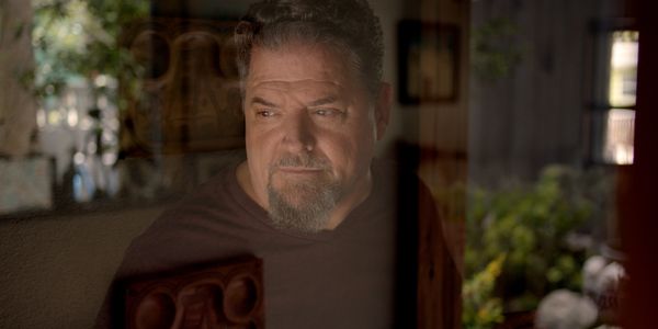 Man with contemplative expression looking through a reflective window.