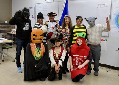 Group of adults in creative Halloween costumes posing in a classroom.