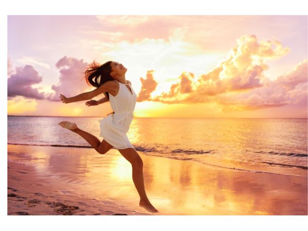 Woman joyfully leaps on the beach at sunset.
