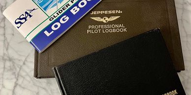 Three pilot logbooks stacked on a marble surface.