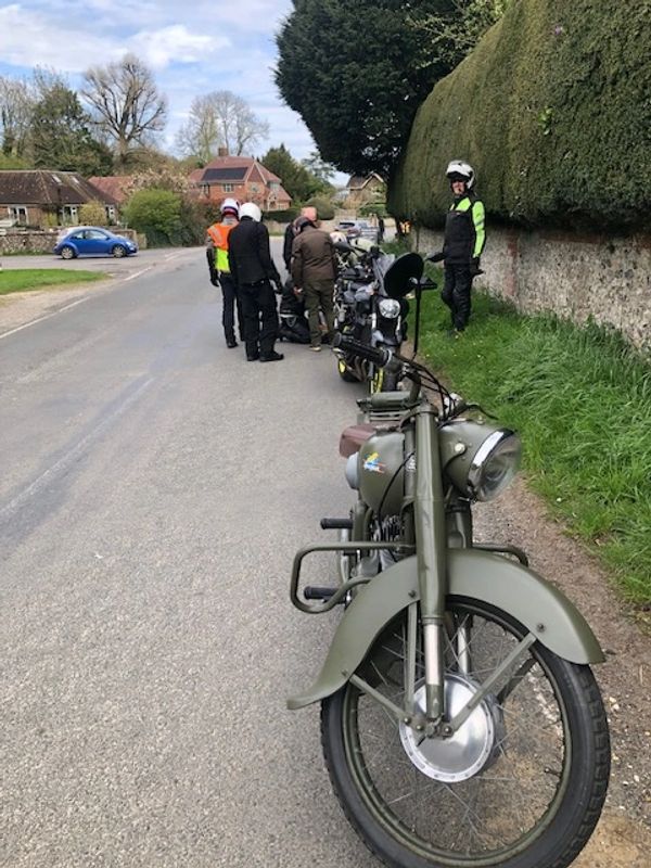 Motorcyclists gathered on a rural road with vintage bikes and safety gear.