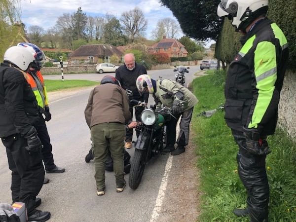 Group of motorcyclists examining a motorcycle by the roadside.