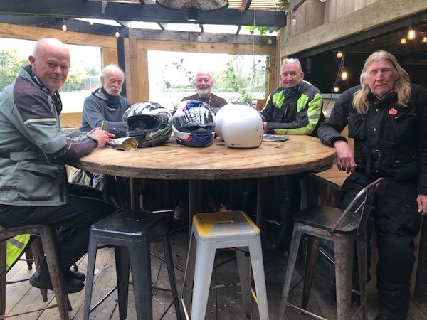 Five men in motorcycle gear sitting around a wooden table with helmets.