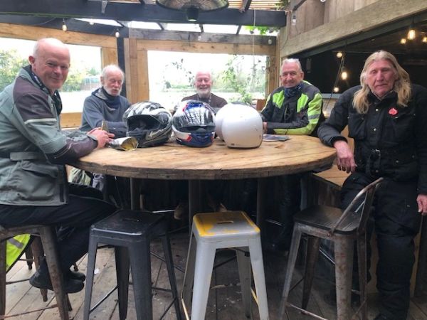 Five men in motorcycle gear sitting around a wooden table with helmets.