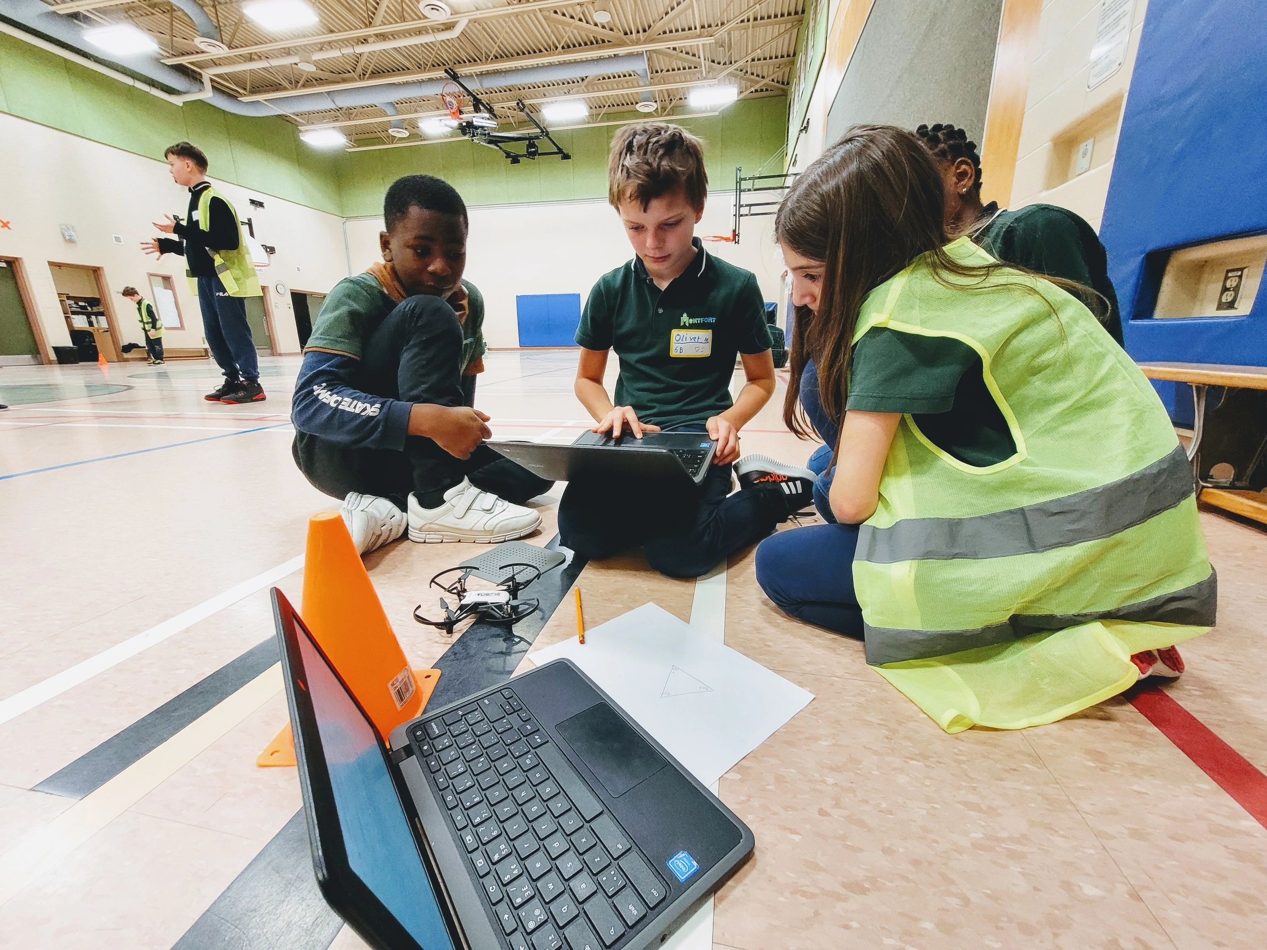 Children working together with laptops and drone in a gym.
