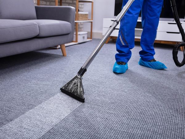 Low Section Of A Male Janitor Cleaning Carpet With Vacuum Cleaning In The Living Room