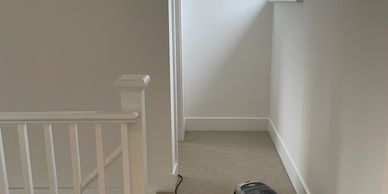 A vacuum cleaner on carpeted floor near white railing and wall.