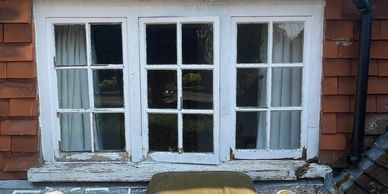 Old window with peeling white paint and a chair outside.