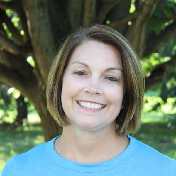 Smiling woman with short hair outdoors near large tree.