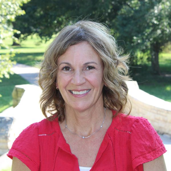 Smiling woman in a red blouse outdoors on a sunny day.