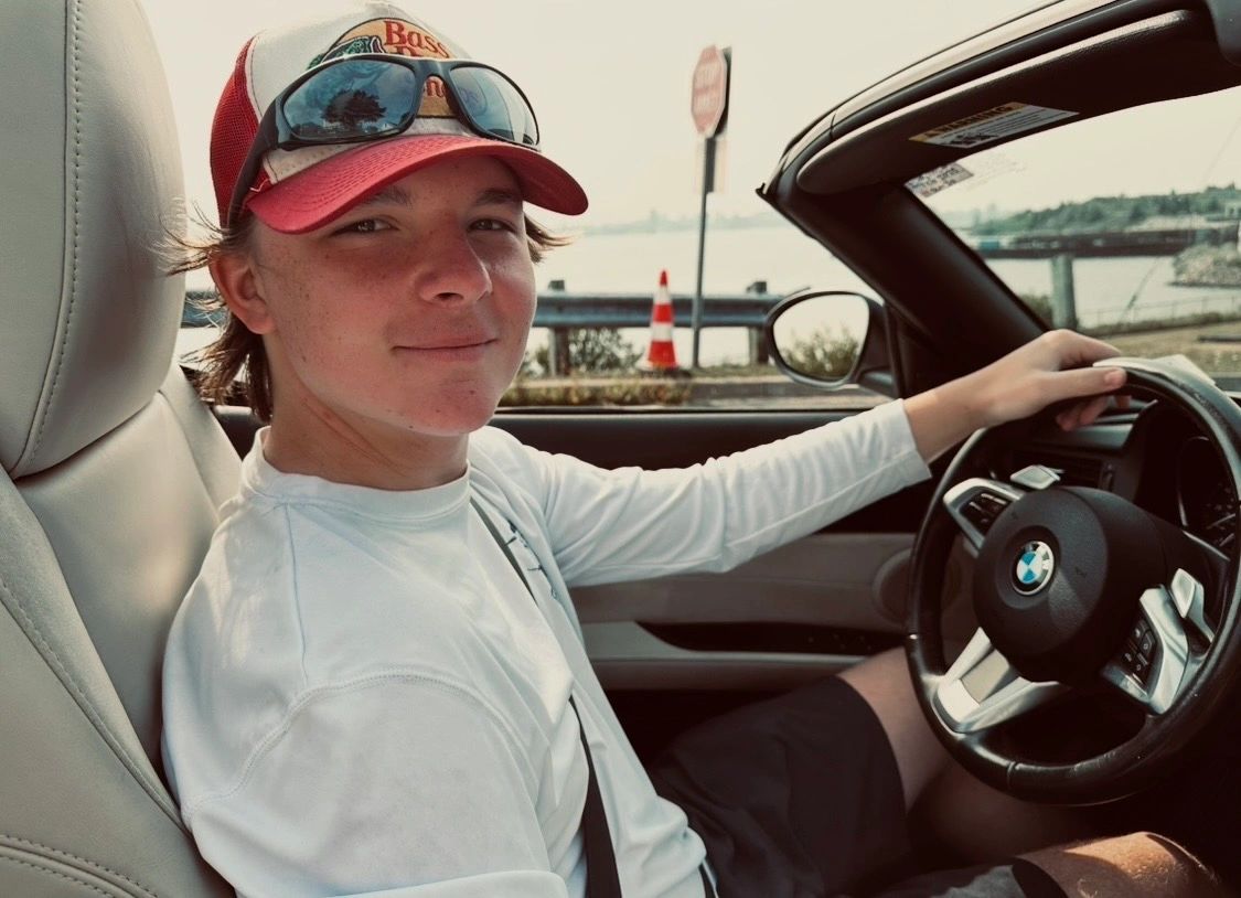 Young man driving a BMW convertible by the water, smiling.
