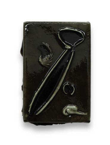 Black soap bar with tie and feather shapes embossed on its surface.