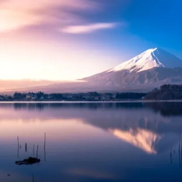 Snow-capped mountain reflected in calm lake at sunrise.